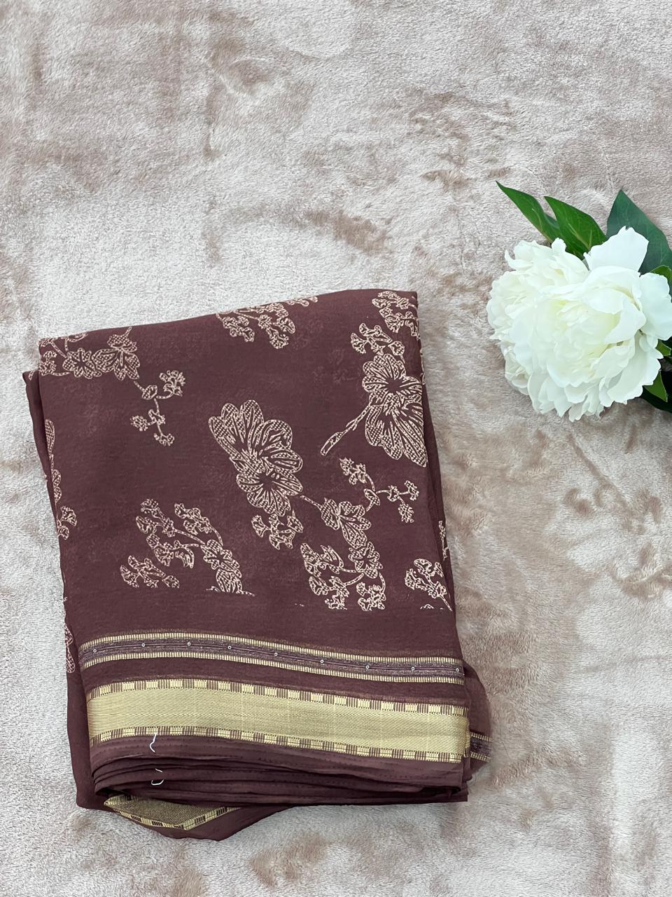 Chocolate brown saree folded flat lay with white peony showing gold zari border
