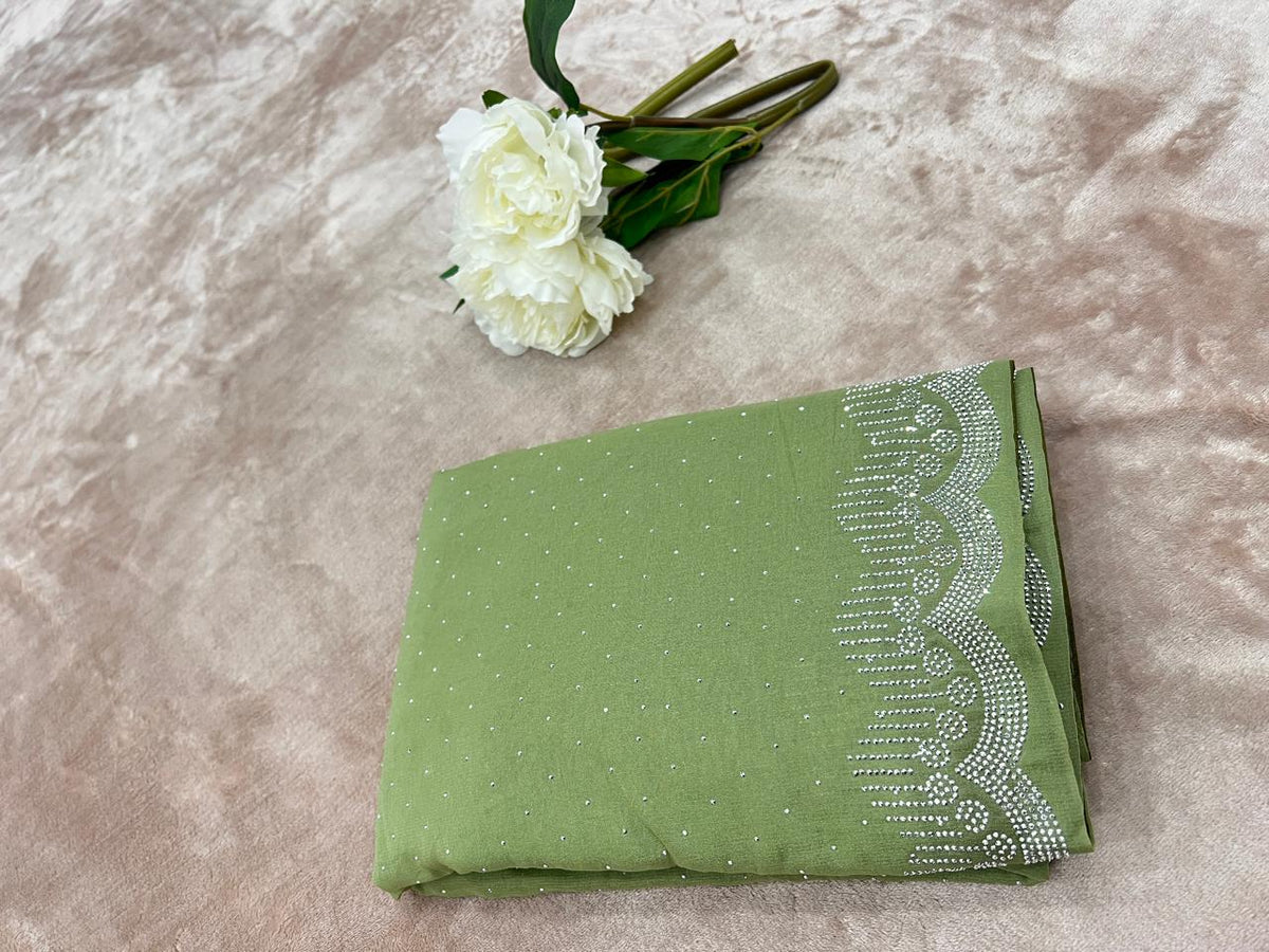 Sage green saree folded flat lay with white peony showing cutdana dot scatter and scallop border