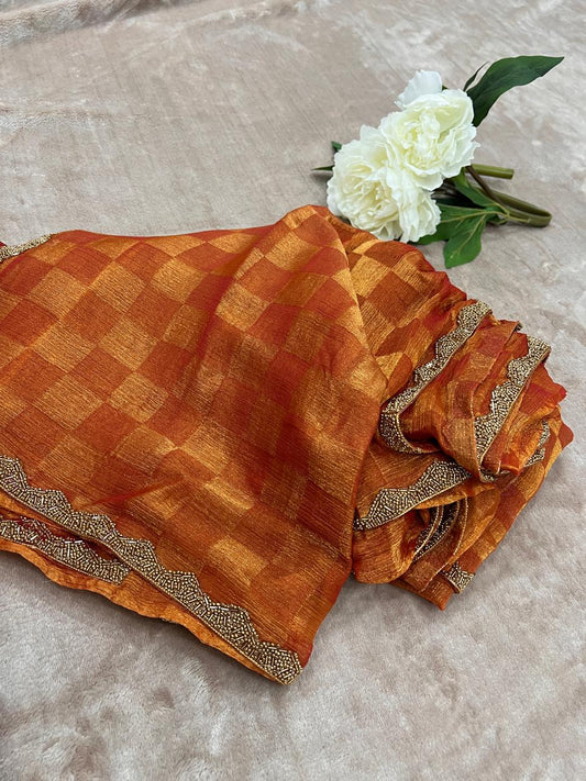 Burnt orange zari check saree flat lay with white peony showing scalloped cutdana border detail